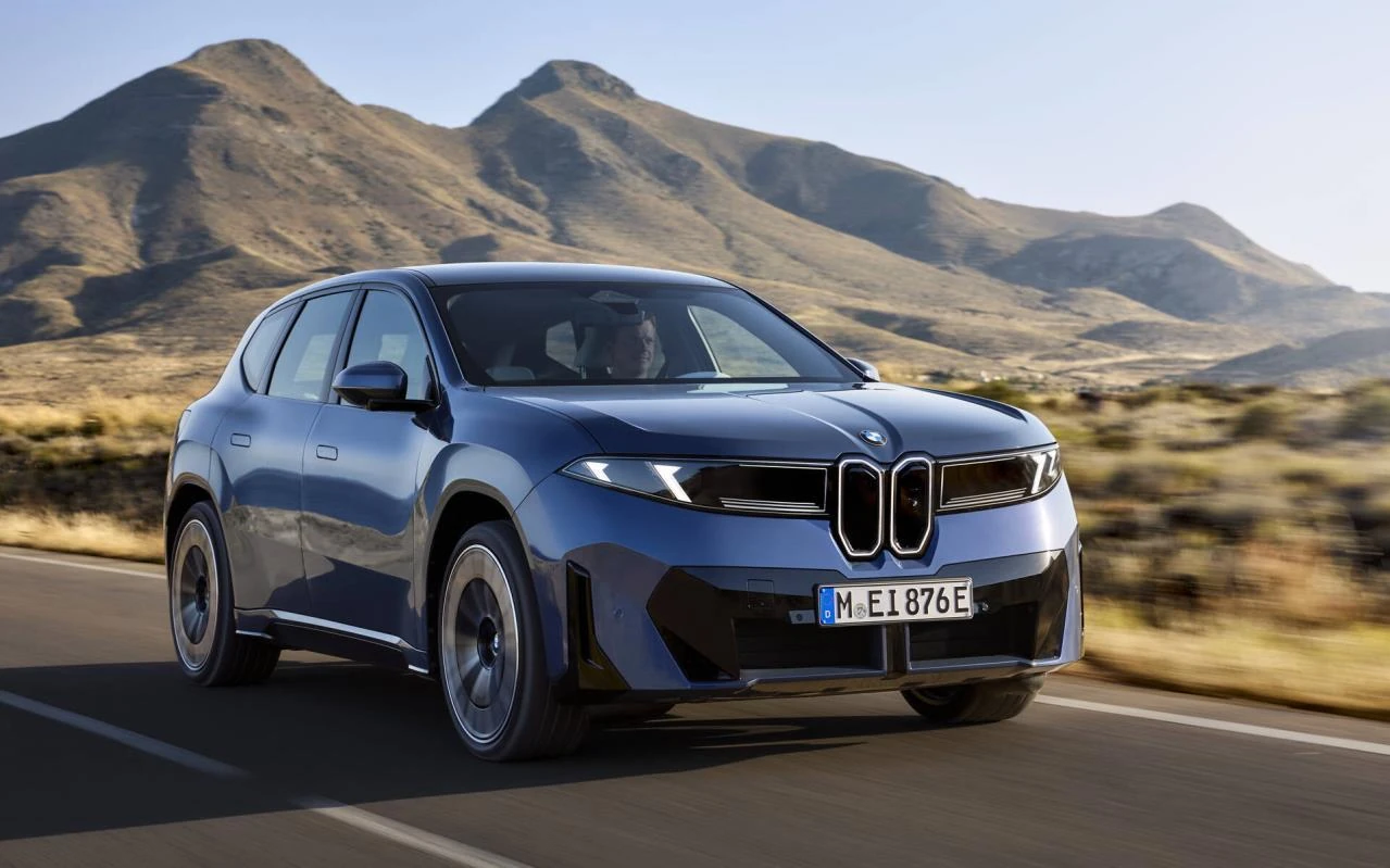 BMW iX3 50 xDrive azul em movimento em uma estrada com montanhas ao fundo.