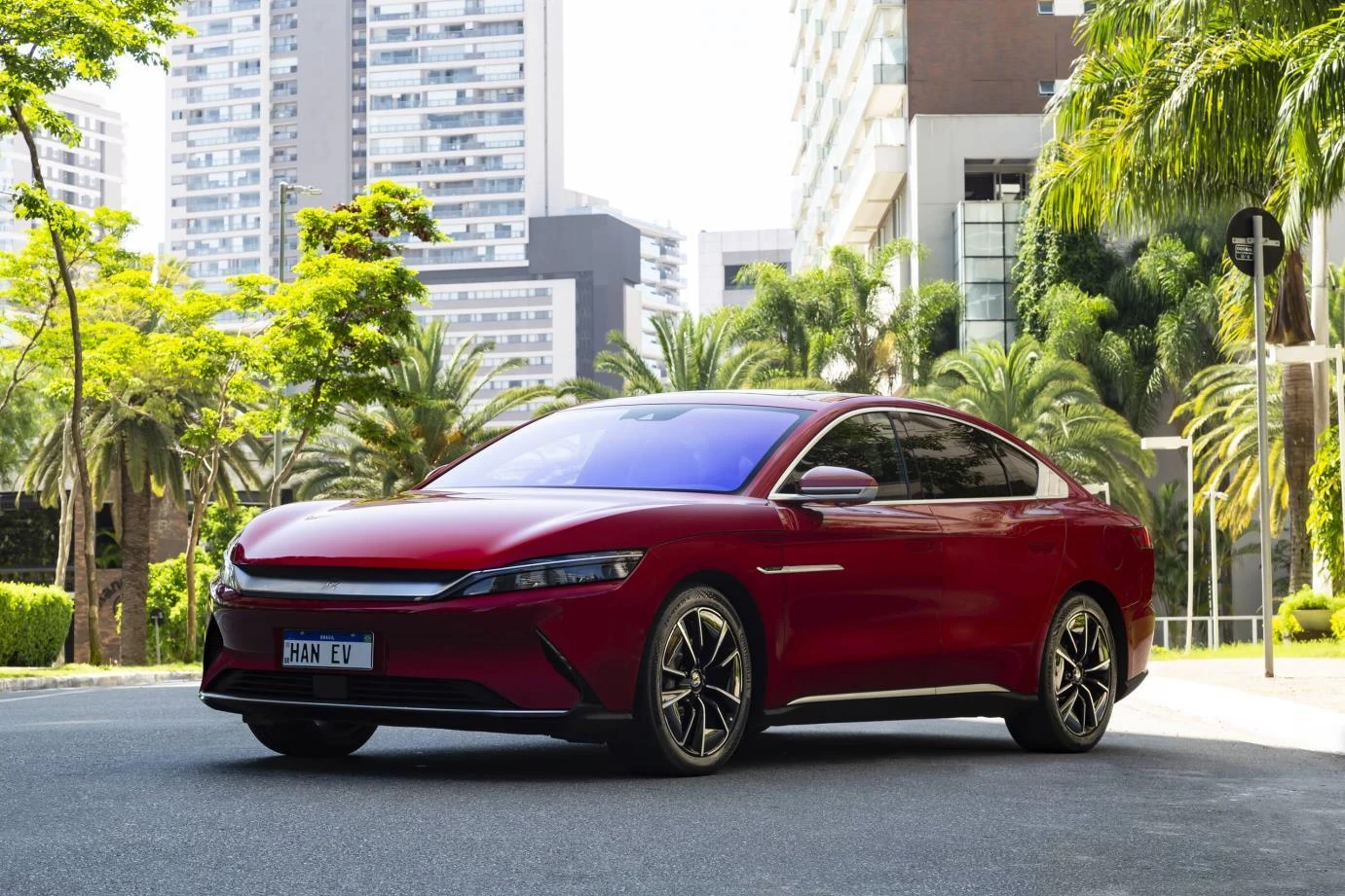BYD Han EV vermelho visto de frente e de lado em uma rua arborizada.