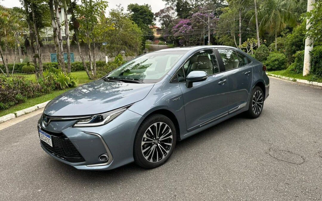 Toyota Corolla Altis Hybrid cinza estacionado em uma rua arborizada.